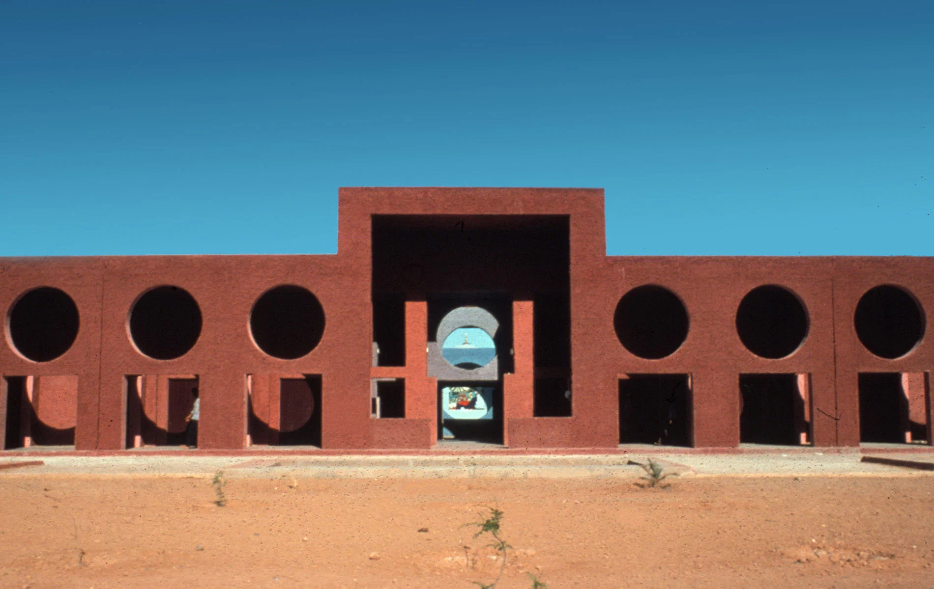 Galería de hormigón rojizo con grandes vanos circulares en el desierto