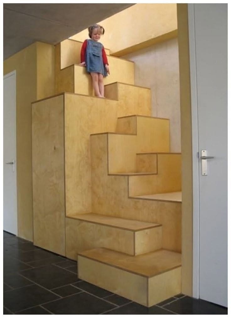 Una niña sentada en lo alto de una escalera de madera integrada a un placard