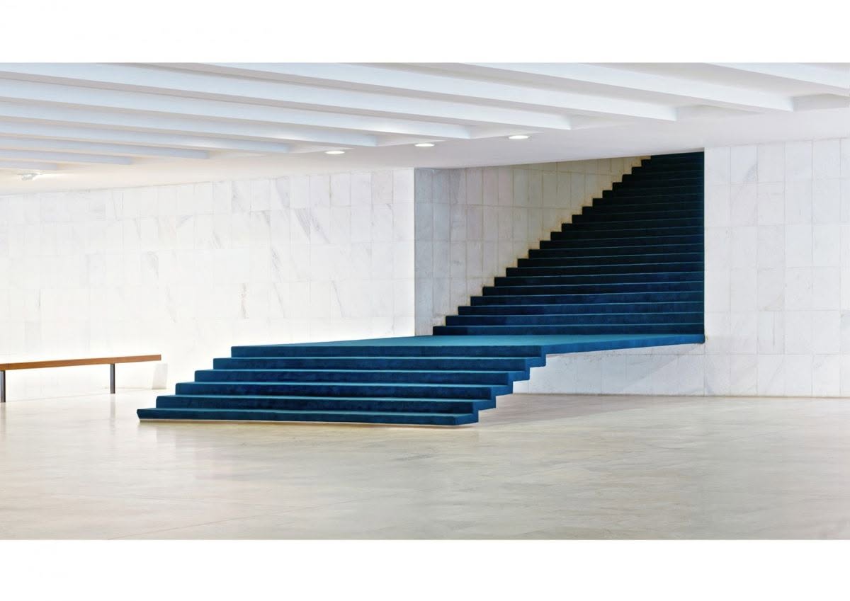 Amplia escalera revestida en azul profundo dentro de un salón de mármol blanco