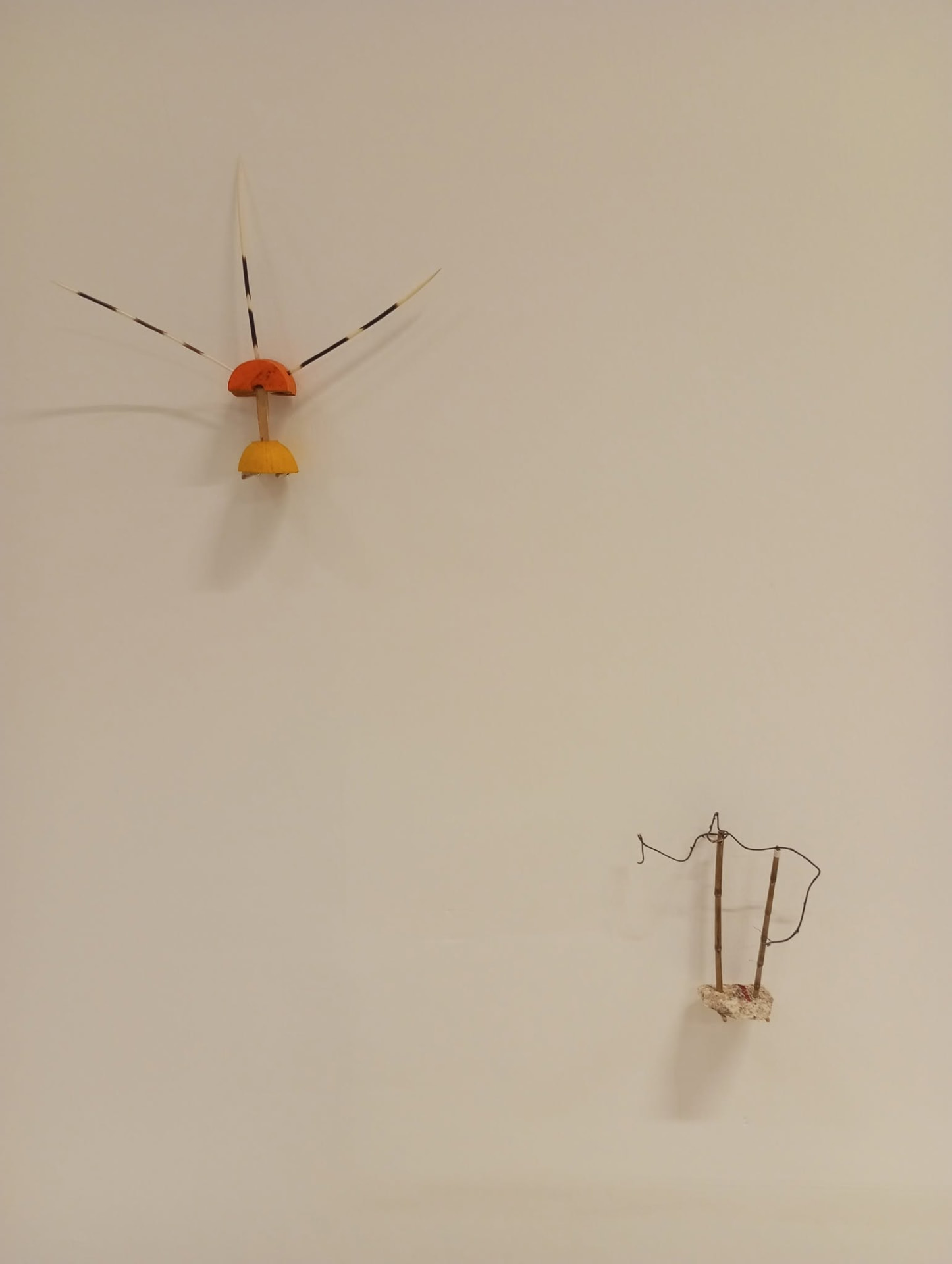 Un micro-ensamble de madera naranja y amarilla con púas de plumas, junto a una pequeña pieza de alambre