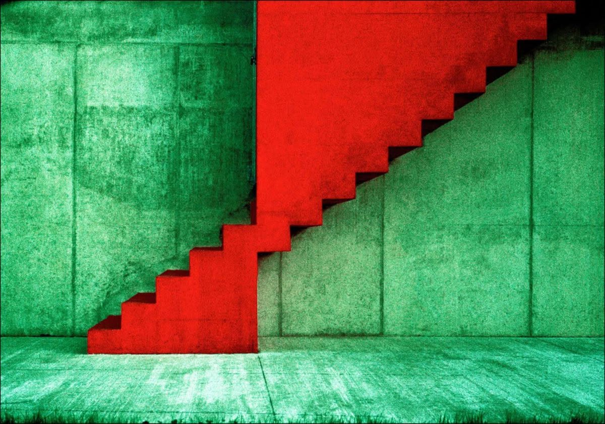 Una escalera roja adosada a un muro de hormigón verdoso
